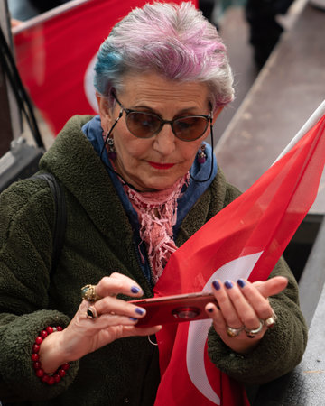 Cankaya, Ankara, Turkey - May 19 2022: An old Turkish woman with dyed hair and her phone and the Turkish flag she's holdingのeditorial素材