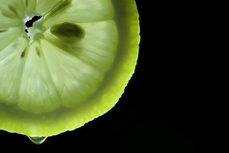 backlit lemon slice on which a drop of juice dripping yellow and sourの写真素材