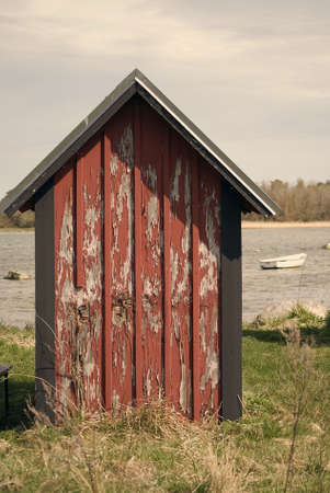Red grunge boathouse with blue sky and water in backgroundの写真素材