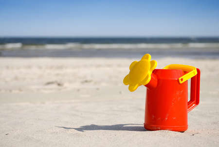 Watering can on tropical sandy beach with ocean in backgroundの写真素材