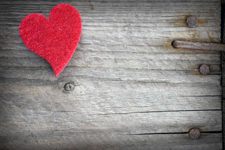 Red heart on old worn vintage board with rusty nailsの写真素材