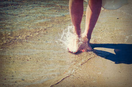 Girl walking barefoot in the water, aged and worn vintage style photoの写真素材