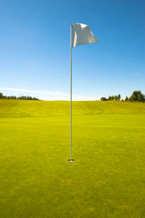 Golf hole with flag, green field and blue skyの写真素材