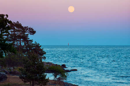 Summer evening with moon and lighthouseの写真素材
