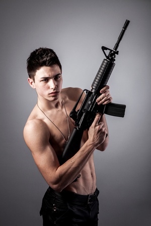 Handsome bare-chested soldier is holding a rifle on black backgroundの写真素材