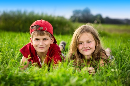 Image of two happy children having fun in the park, brother and sister lying down on green grass, best friends playing outdoors in spring, adorable little girl with cute boy enjoying springtime natureの写真素材
