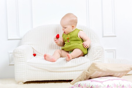little kid sit on a sofa and eating strawberriesの写真素材