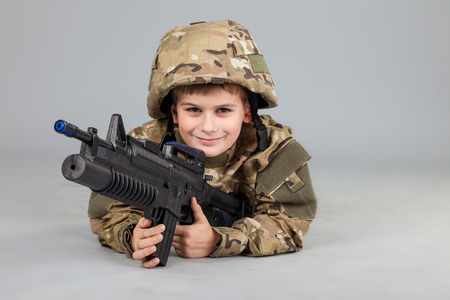 Young boy dressed like a soldier with rifle isolated on gray backgroundの写真素材