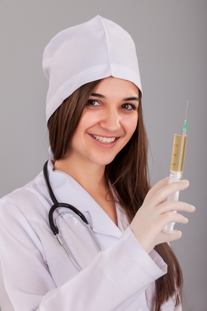 Woman doctor holding a filled syringe in hand on grey backgroundの写真素材