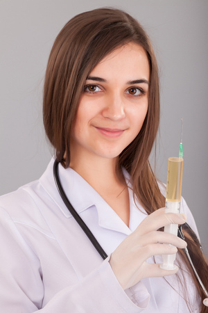 Woman doctor holding a filled syringe in hand on grey backgroundの写真素材