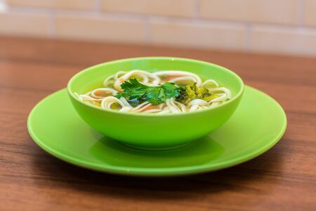 Chicken soup with macaroni in a green plate on a wooden tableの写真素材