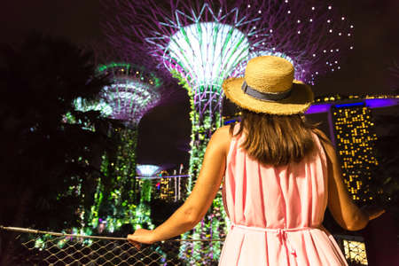 SINGAPORE, SINGAPORE - FEBRUARY 26, 2020: Woman traveler looking at Gardens by the Bay and Marina Bay Sands Hotel at night in Singaporeのeditorial素材