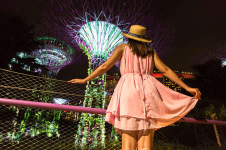 SINGAPORE, SINGAPORE - FEBRUARY 26, 2020: Woman traveler looking at Gardens by the Bay and Marina Bay Sands Hotel at night in Singaporeのeditorial素材
