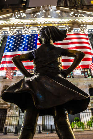 NEW YORK CITY, USA - MARCH 15, 2020:  Fearless Girl Statue looking up at  New York Stock Exchange building at Wall Street in Manhattan at night, New York City, USAのeditorial素材