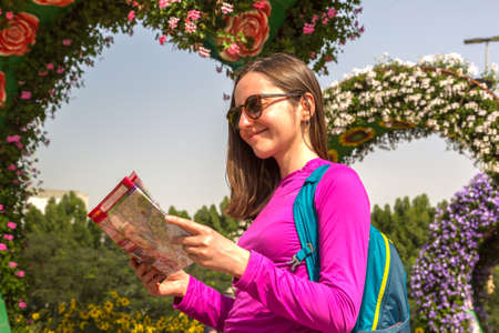 DUBAI, UNITED ARAB EMIRATES - JANUARY 31, 2020: Happy girl traveler looks at the map while walking in Dubai miracle garden in a sunny day , United Arab Emiratesのeditorial素材