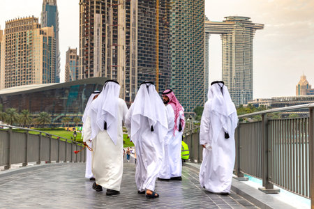 DUBAI, UAE - APRIL 5, 2020: Arabic men wearing traditional white clothes walking in Dubai downtown,...