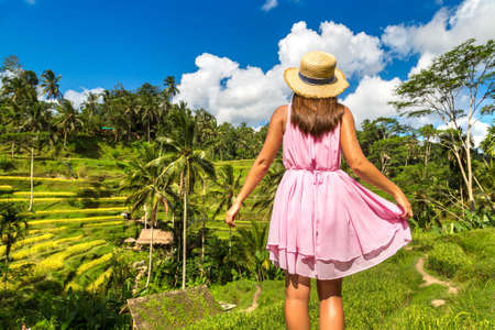 Woman traveler wearing pink dress and straw hat at  Tegallalang rice terrace field on Bali, Indonesia in a sunny day