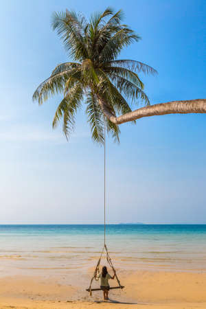 Beautiful woman swinging on palm tree over luxury tropical beach in a sunny summer dayの写真素材