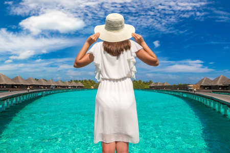Beautiful young woman in front of water luxury villas standing on the tropical beach jetty (wooden pier) in Maldives islandの写真素材