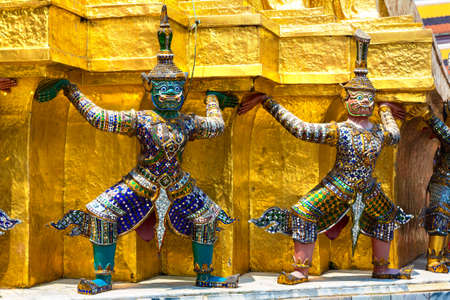 Demon Guardian Statues are supporting golden Chedi stupa at Wat Phra Kaew temple in a sunny dayの写真素材