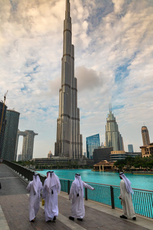 DUBAI, UAE - APRIL 5, 2020: Arabic men wearing traditional white clothes walking in Dubai downtown against Burj Khalifa tower, United Arab Emiratesのeditorial素材
