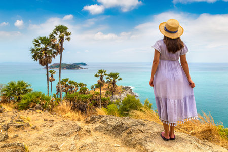 Woman traveler wearing blue dress and straw hat at   Phromthep Cape at Phuket in Thailand in a...