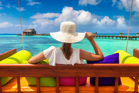 Beautiful woman is sitting on swing at luxury tropical beach in a sunny summer dayの写真素材
