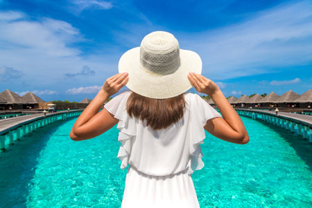 Beautiful young woman in front of water luxury villas standing on the tropical beach jetty (wooden pier) in Maldives islandの写真素材