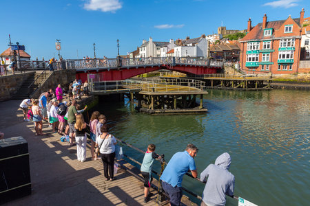 WHITBY, UK - JUNE 29, 2025: Families and tourists crabbing along the harbour wall in Whitby on a summer day in North Yorkshire, England, United Kingdomのeditorial素材