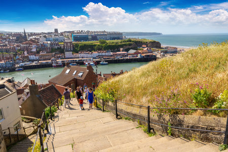 WHITBY, UK - JUNE 29, 2025: Visitors walking up the famous 199 Steps with panoramic view of Whitby Harbour and coastline in Whitby, North Yorkshire, England, United Kingdomのeditorial素材