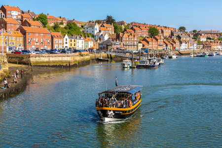 WHITBY, UK - JUNE 29, 2025: Black Pearl Pirate Boat Trips sailing through Whitby Harbour past historic waterfront buildings in North Yorkshire, England, United Kingdomのeditorial素材