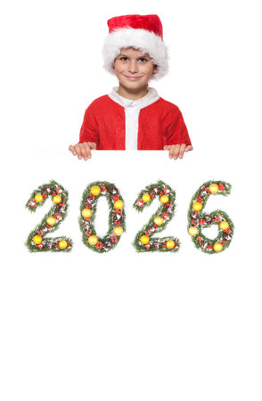 Smiling boy dressed as Santa Claus holding Christmas poster with 2026 number made from evergreen branches with ornaments isolated on white backgroundの写真素材