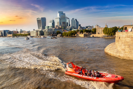 LONDON, UK - SEPTEMBER 21, 2024: Red Thames Rockets speedboat on River Thames with Tower of London castle and modern skyscrapers of financial district in City of London, England, United Kingdom at sunsetのeditorial素材