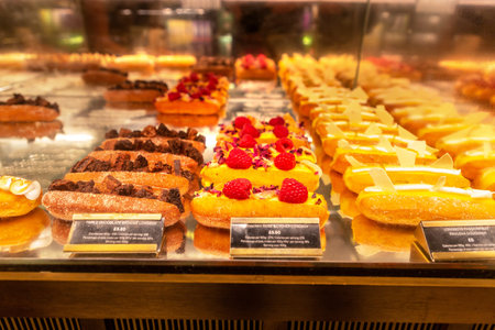 LONDON, UK - AUGUST 26, 2024: Assorted gourmet doughnuts with chocolate and raspberry toppings on display in glass bakery counter at Harrods Food Hall in Knightsbridge, London, England, United Kingdomのeditorial素材