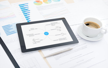 Modern digital tablet with business plan on screen, cup of coffee and some papers and documents with...