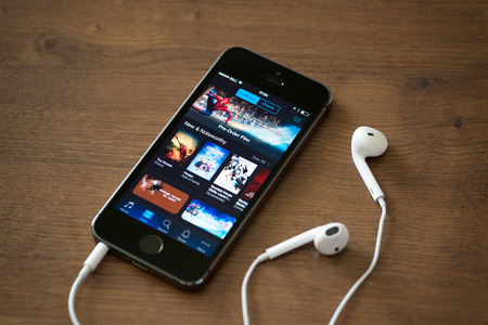 KIEV, UKRAINE - JUNE 05, 2014: Brand new Apple iPhone 5S with iTunes store application on the screen lying on a desk with headphones. iTunes is the media library with player for download and organize media files, developed by Apple Inc.のeditorial素材
