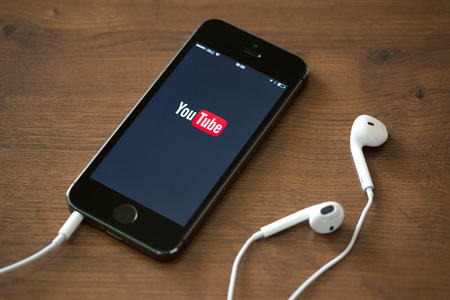 KIEV, UKRAINE - JUNE 05, 2014: Brand new Apple iPhone 5S with YouTube application service on the screen lying on a desk with headphones. YouTube is the world's most popular online video-sharing website that founded in February 14, 2005のeditorial素材