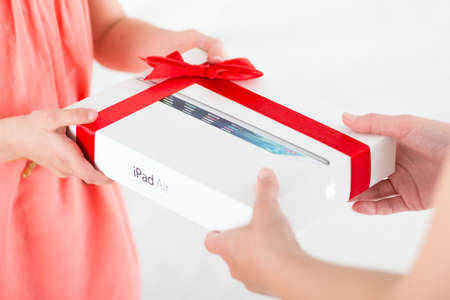 KIEV, UKRAINE - MAY 30, 2014: Mother gives her daughter a birthday present â brand new Apple iPad Air in a festive packaging. Apple iPad Air developed by Apple inc. and was released on November 1, 2013.のeditorial素材
