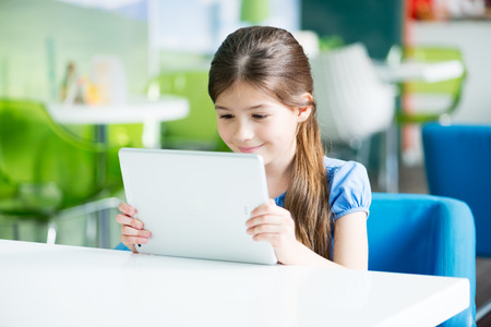 KIEV, UKRAINE - MAY 21, 2014: Little smiling  girl sitting at the desk and looking on a brand new Apple iPad Air. Apple iPad Air developed by Apple inc. and was released on November 1, 2013.のeditorial素材