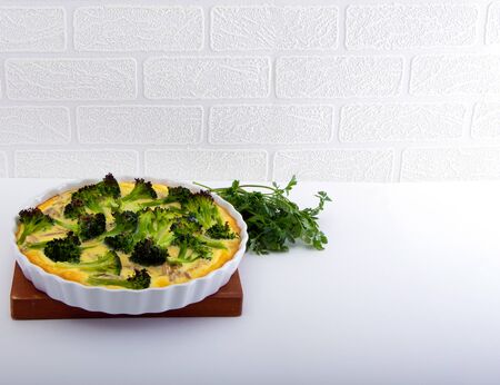 Baked Quiche with Broccoli, Onion, Meat and Bacon in White Ceramic Dish on White Background.の写真素材