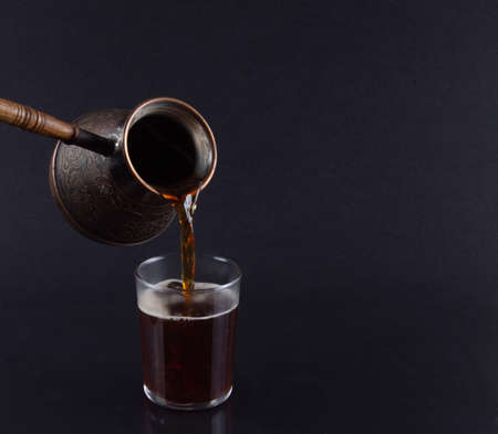 Freshly Brewed Turkish Coffee Poured from Cezve into Glass on Dark Background.の写真素材