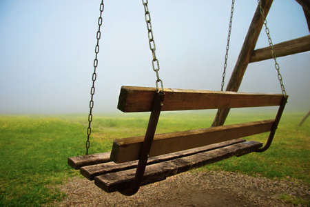 abandoned wooden bench on chains in mysterious fogの写真素材