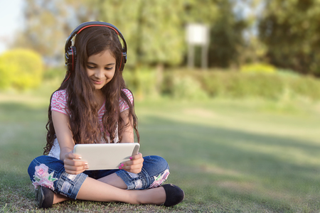 Girl Playing Tablet Wearing Wireless Headphones. Ten Years Old Girl Listen Music and Playing Games on the Tablet Device. vertical composition.の写真素材