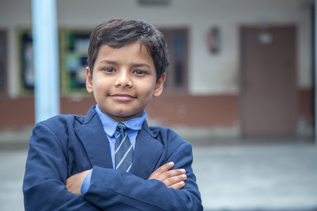 Closeup portrait of smiling 6-7 years Indian kid, standing straight at school campus in school uniform and looking at cameraの写真素材
