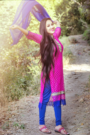 Woman with long hair and beautiful eyes on a green background wearing Indian suit and dupatta. Lady portrays dancing, jumping, fun, happiness, smileの写真素材