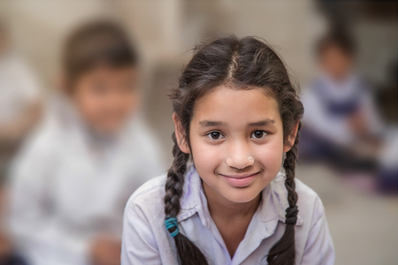 Girl sitting on the floor of her government primary school in uniform along with some of her class mates sitting behind her. Selective focus, shallow depth of field.の写真素材