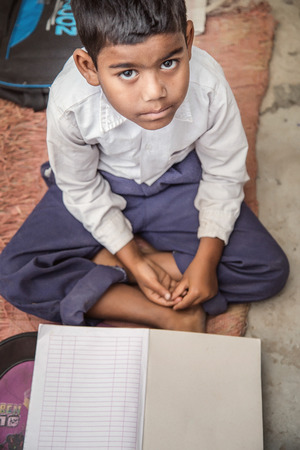 School boy sitting on the floor of primary school in uniform having his note book in front of him. Selective focus, shallow depth of field.の写真素材