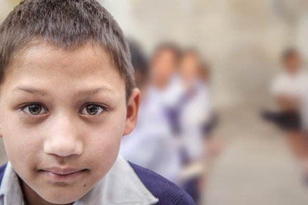 Boy sitting on the floor of government primary school in uniform along with some of his class mates...