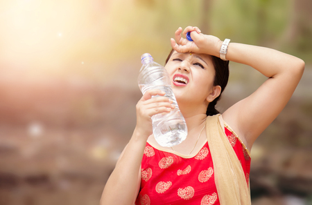 Young Indian woman holding water bottle during warm sunny day.の写真素材