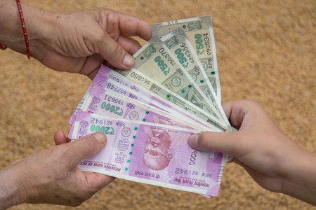 Hand Giving Indian 500 and 2000 Rupee Bank Notes over wheat background.